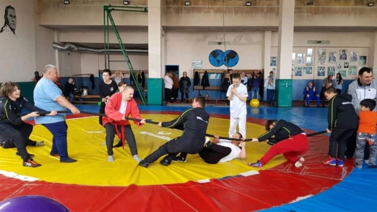 Деца и възрастни тренират самбо в спортна зала.